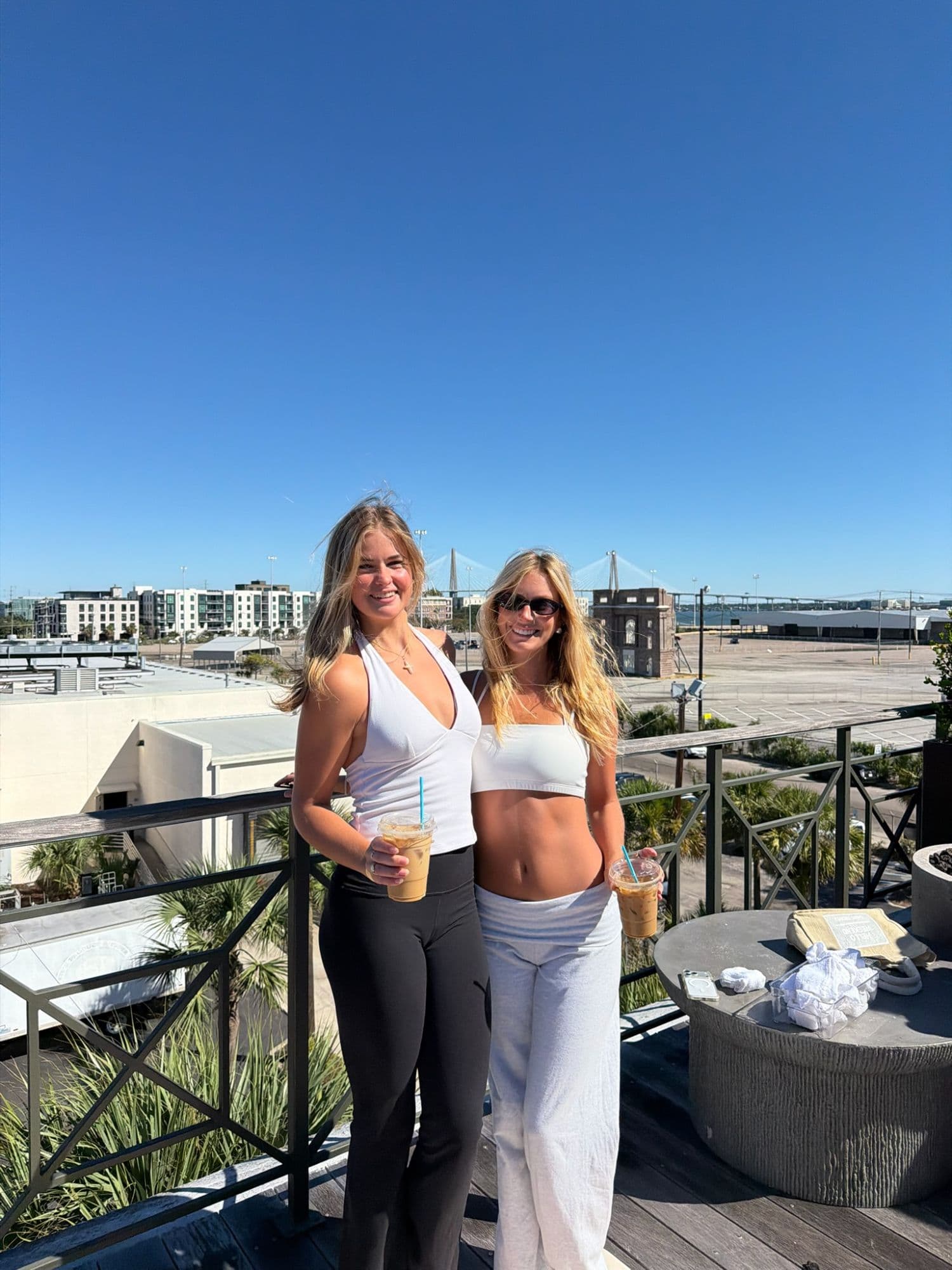 Two guests with iced coffees on the Ansonborough rooftop, Charleston skyline behind them