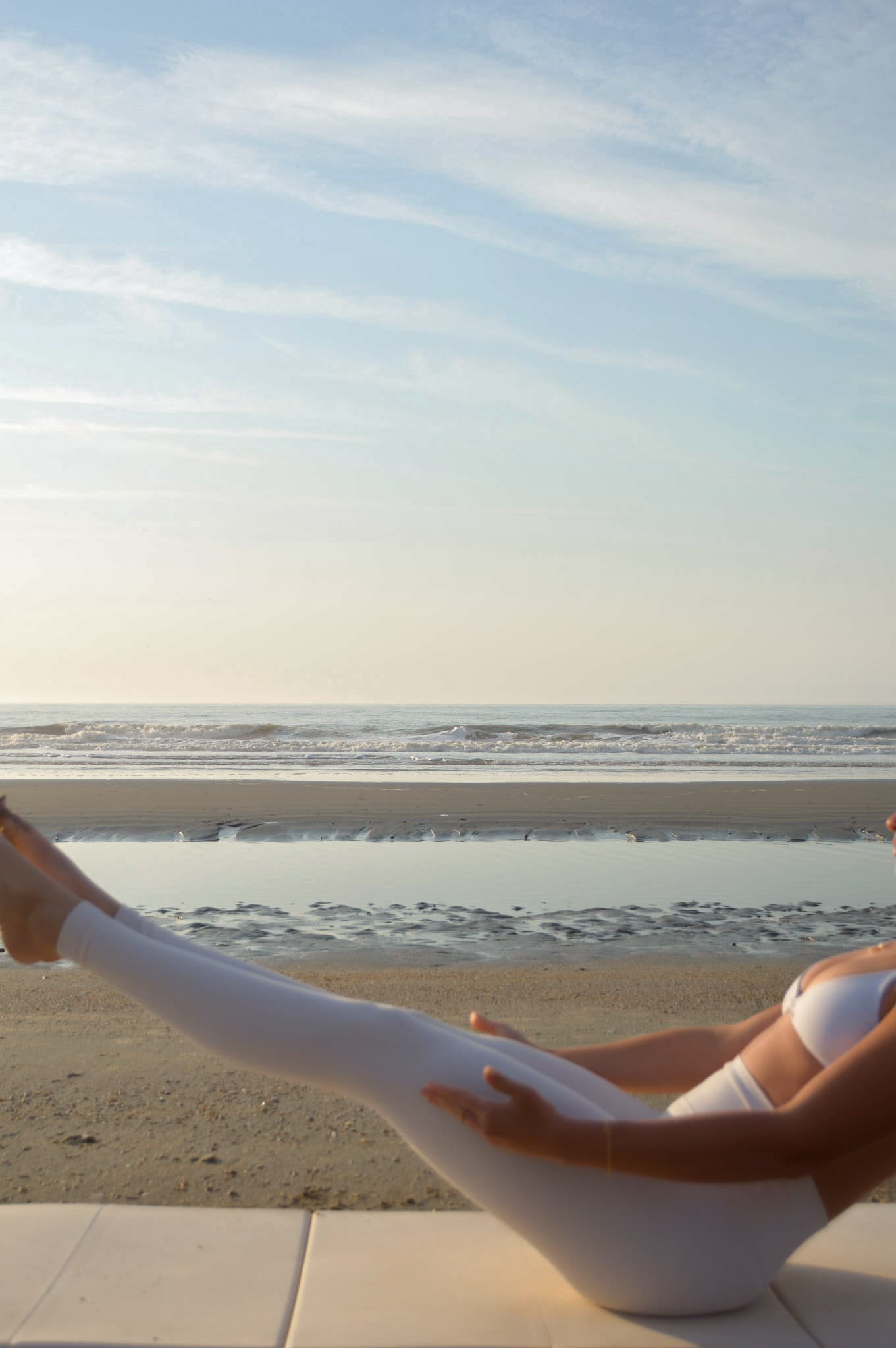 Halle in a Pilates pose at the beach at golden hour, ocean horizon behind her